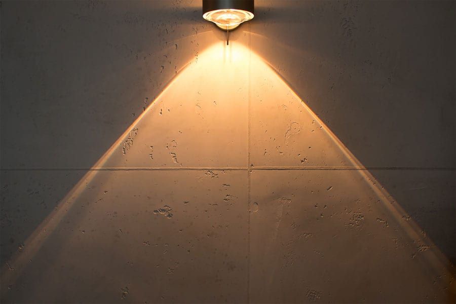 Detailaufnahme eines warmen Lichtkegels auf handgefertigtem Kalkputz in Beton-Optik.