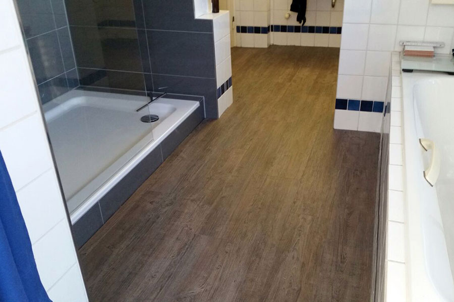 Neuer Badezimmerboden in Holzoptik neben Dusche und Badewanne.