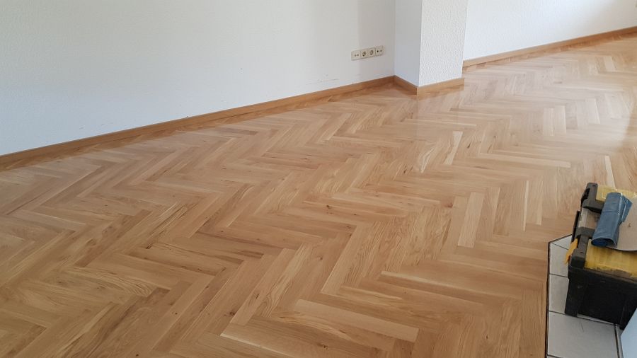 Eiche massiv Parkett, 22mm stark, im Fischgrat Verband verlegt und endbehandelt. Inkl. Fußleistenmontage.